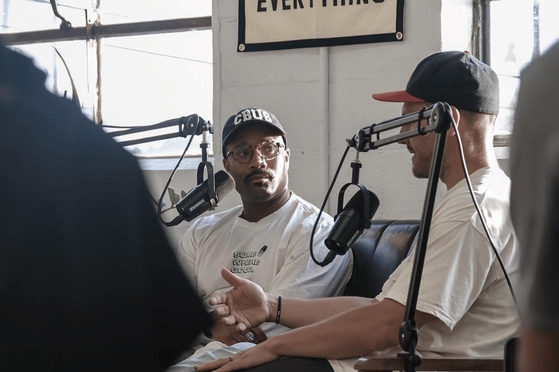 An African American man and Caucasian man having a lively conversation while recording a podcast in a studio.