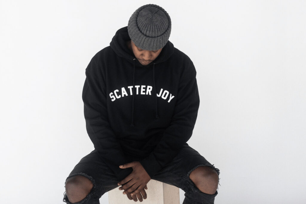 Young African American man with a gray beanine—wearing a black scatter joy project sweatshirt.