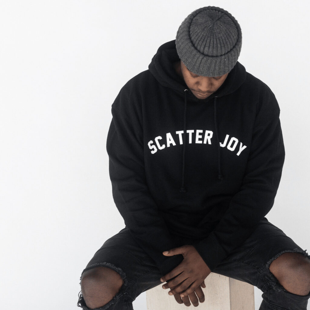 Young African American man with a gray beanine—wearing a black scatter joy project sweatshirt.